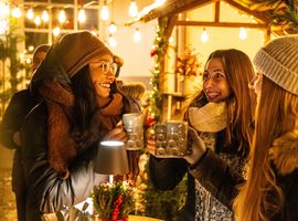 Drei Frauen stoßen mit Glühwein auf dem weihnachtlich geschmückten Platzl-Hof an