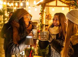 Drei Frauen stoßen mit Glühwein auf dem weihnachtlich geschmückten Platzl-Hof an