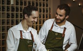 Two happy restaurant staff members wearing green aprons and white shirts, with a friendly and professional appearance in the photo
