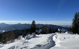 Snowy hiking trail leading to a hut with mountains and blue sky in the background