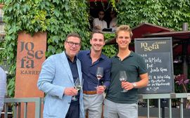 Drei Männer mit Wein vor Josefa Karriere-Schild im Grünen