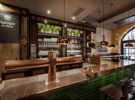 The Ayinger am Platzl bar with copper beer taps, green tiles and hanging brass lamps