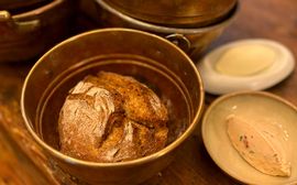 Frisches Bauernbrot liegt in einem Kupfertopf, daneben stehen Butter und ein würziger Aufstrich