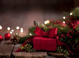 Geschenk Rot eingepacktes Geschenk vor Tannenzweigen und weihnachtlicher Dekoration.