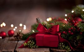 Rot eingepacktes Geschenk vor Tannenzweigen und weihnachtlicher Dekoration.