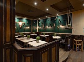 Gemütlicher Essbereich mit Holzvertäfelung, grüner Dekoration und quadratischen Tischen mit schlichter Tischdekoration