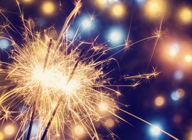 Eine Wunderkerze sprüht funkelnde Lichter vor einem bunten, festlichen Hintergrund