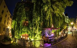 Grün bewachsenes und beleuchtetes Karree Boden & Bar bei Nacht in München