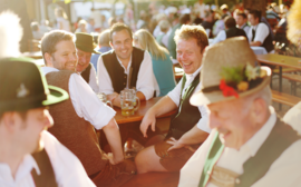 Mehrere Männer unterhalten sich im Biergarten des Ayinger Bräustüberls.