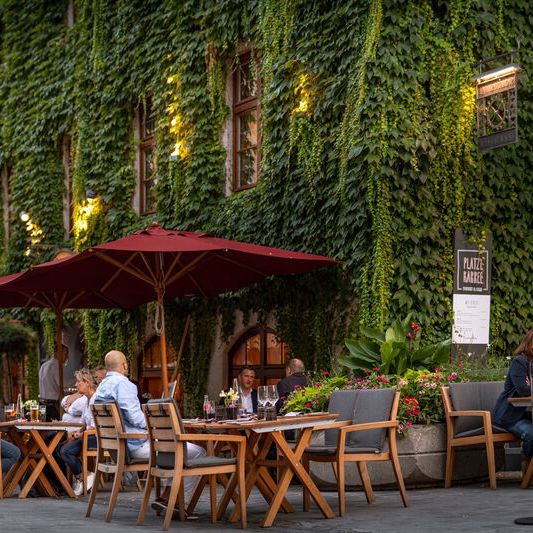 Außenbereich der Pfistermühle an dem Gäste Essen und Trinken unter einem Gartenschirm genießen.